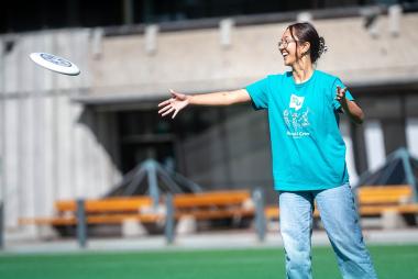 Woman joyfully throwing a frisbee on a sunny day at a campus field