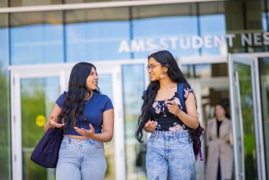 Two students talking and smiling while walking outside a university building.